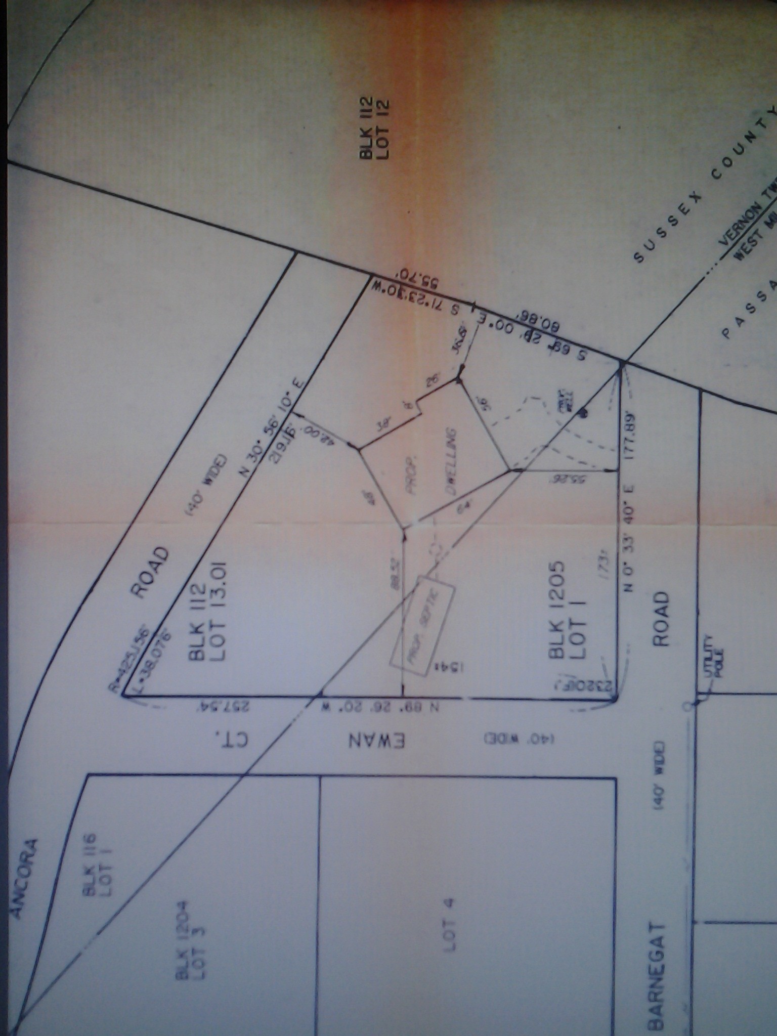 Image: There are hand drawn blue lines outlining an irregular quadrilateral for 89 Barnegat Road that encloses a forward diagonal line separating two counties: Sussex Block 12 Lot 13.01 and Passaic Block 1205 Lot 1.  Rotating clockwise from top, this irregular quadrilateral is surrounded by Block 112 and Lot 12, Barnegat Road, Ewan Court and Ancora Road.  Below Ewan Court, right to left, are Lot 4, Block 1204 Lot 3, a forward diagonal line separating two counties: Sussex and Passaic, and Block 116 Lot 1.  Each Road is 40 feet wide.